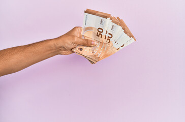 Hispanic hand holding 50 euro banknotes over isolated pink background.