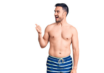 Young handsome man wearing swimwear smiling with happy face looking and pointing to the side with thumb up.