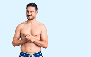 Fototapeta premium Young handsome man wearing swimwear with hands together and crossed fingers smiling relaxed and cheerful. success and optimistic