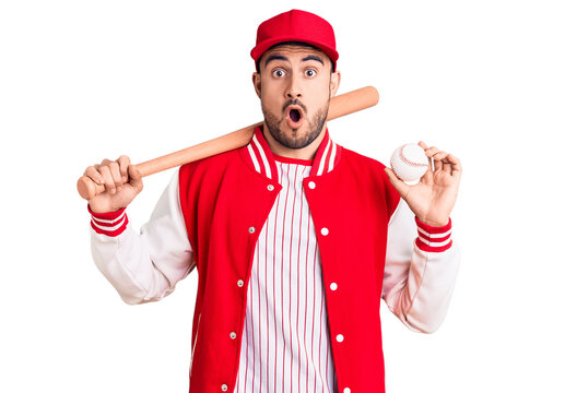 Young handsome man holding baseball bat and ball scared and amazed with open mouth for surprise, disbelief face