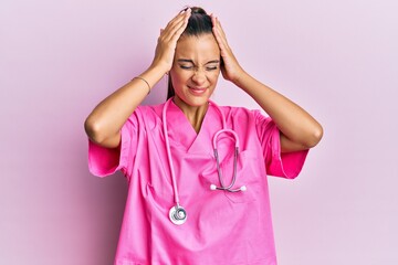 Young hispanic woman wearing doctor uniform and stethoscope suffering from headache desperate and stressed because pain and migraine. hands on head.