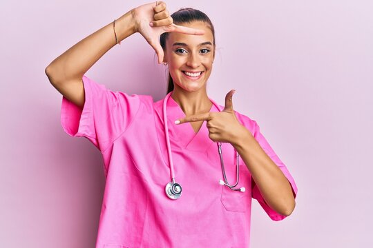 Young hispanic woman wearing doctor uniform and stethoscope smiling making frame with hands and fingers with happy face. creativity and photography concept.