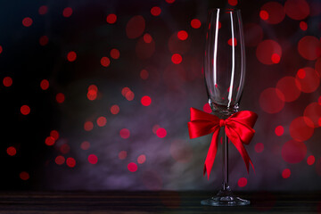 Champagne Flute Glass decorated with red silk ribbon bow. Beautiful bokeh on background. Festive mood on  Valentines day or Christmas.