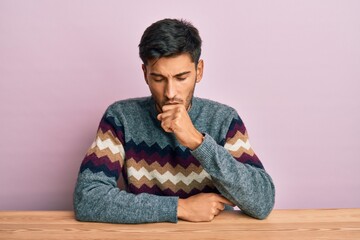 Young handsome man wearing casual winter sweater sitting on the table feeling unwell and coughing as symptom for cold or bronchitis. health care concept.