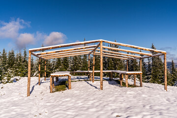 The gazebo on the top of the mountain stands in a snow-covered meadow, bathed in the light of the bright cold sun