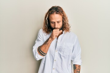 Handsome man with beard and long hair wearing casual white shirt feeling unwell and coughing as...