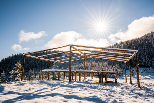 The gazebo on the top of the mountain stands in a snow-covered meadow, bathed in the light of the bright cold sun