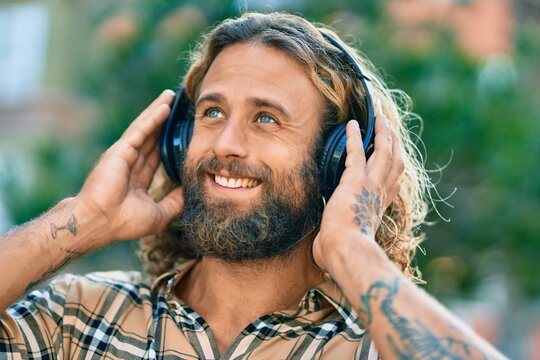 Young caucasian man smiling happy using headphones at the park.