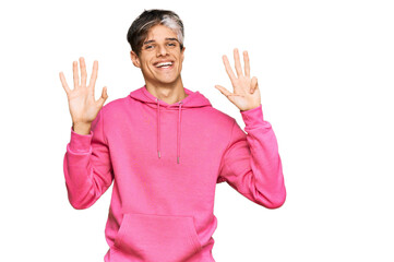 Young hispanic man wearing casual pink sweatshirt showing and pointing up with fingers number nine...