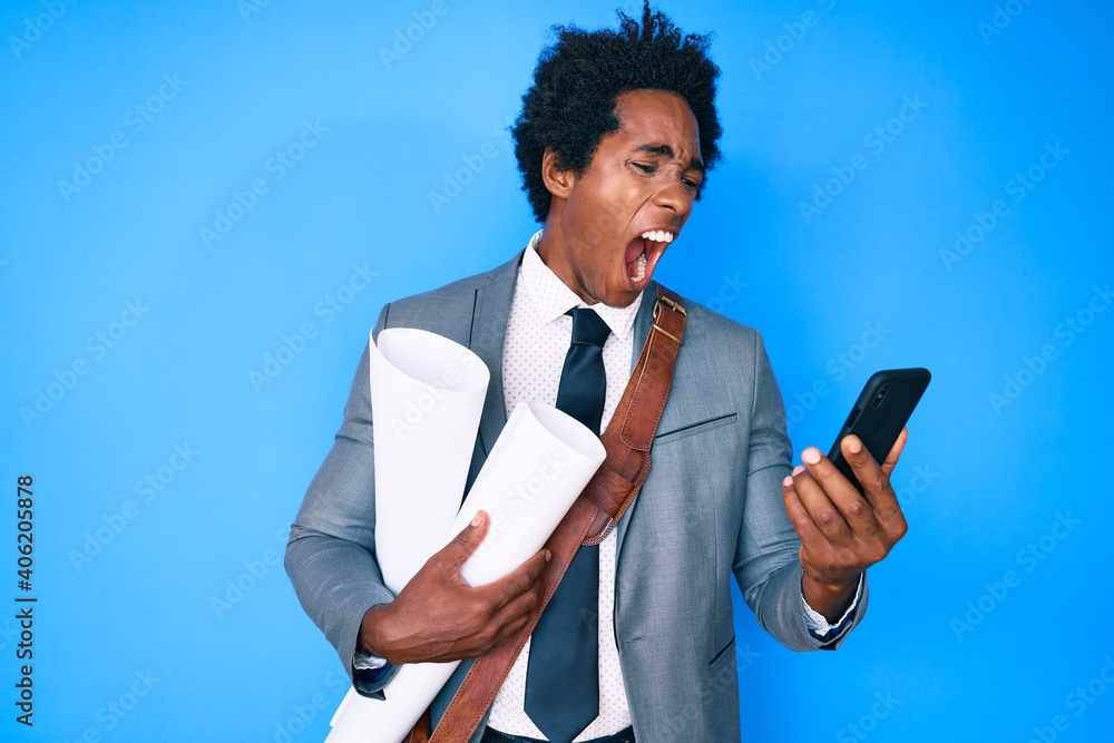 Poster handsome african american man with afro hair holding paper blueprints using smartphone angry and mad