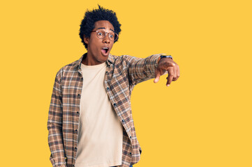 Handsome african american man with afro hair wearing casual clothes and glasses pointing with...