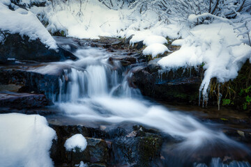 Small stream among wet stones and white snow in the picturesque Carpathian mountains in Ukraine