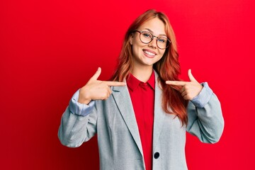 Young redhead woman wearing business jacket and glasses looking confident with smile on face, pointing oneself with fingers proud and happy.