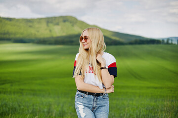 Cute blonde model in pink sunglasses smiling and posing outdoors with the beautiful landscape in the background