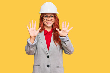 Young redhead woman wearing architect hardhat showing and pointing up with fingers number ten while...