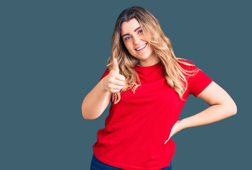 Young caucasian woman wearing casual clothes doing happy thumbs up gesture with hand. approving expression looking at the camera showing success.