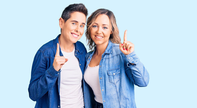 Couple of women wearing casual clothes pointing finger up with successful idea. exited and happy. number one.