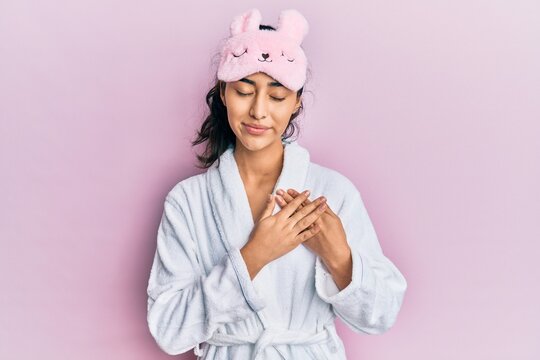 Hispanic teenager girl with dental braces wearing sleep mask and robe  smiling with hands on chest with closed eyes and grateful gesture on face.  health concept. Stock Photo