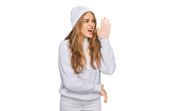 Young caucasian girl wearing wool sweater and winter cap shouting and screaming loud to side with hand on mouth. communication concept.
