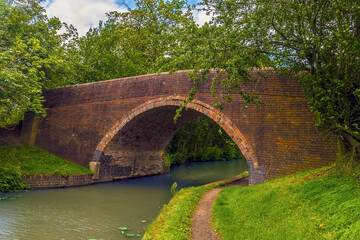 Fototapeta na wymiar A Victorian brick-built bridge spans the Grand Union Canal near Wistow, UK in summertime