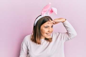 Young beautiful woman wearing cute easter bunny ears very happy and smiling looking far away with hand over head. searching concept.