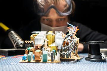 A man in glasses and a mask, with a soldering iron, repairs equipment