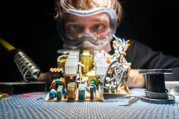 A man in glasses and a mask, with a soldering iron, repairs equipment