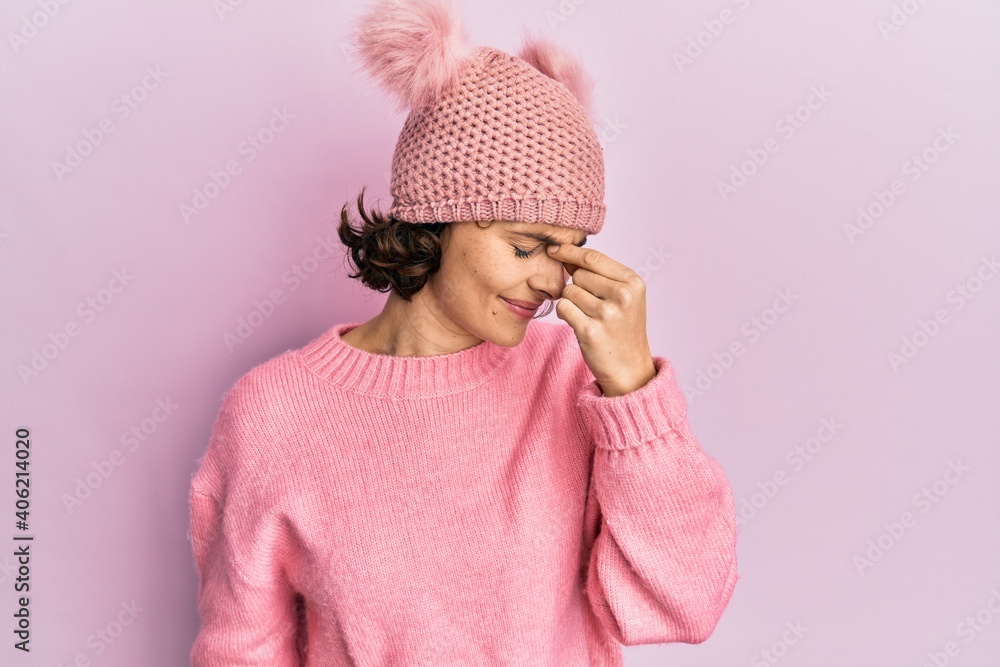 Sticker young brunette woman wearing cute wool cap tired rubbing nose and eyes feeling fatigue and headache.