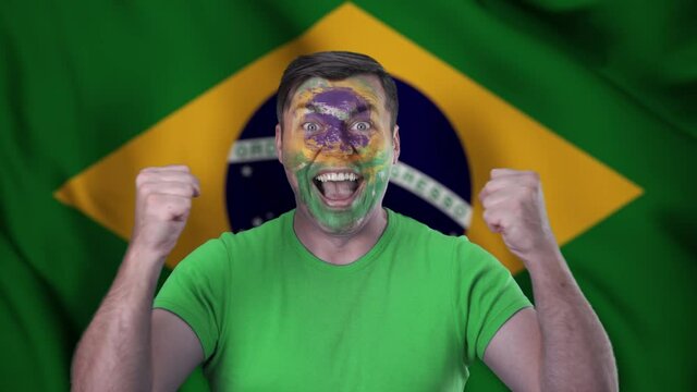 A screaming Brazilian cheerleader with a face painted in the color of the Brazilian flag.