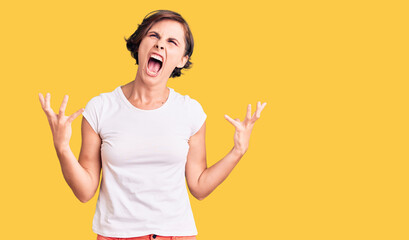 Beautiful young woman with short hair wearing casual clothes crazy and mad shouting and yelling with aggressive expression and arms raised. frustration concept.