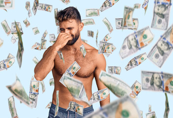Young hispanic man wearing swimwear shirtless smelling something stinky and disgusting, intolerable...