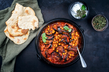Modern style slow cooked Lebanese vegetarian eggplant stew maghmour served with chickpeas and pita bread as top view in a design pot