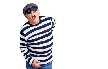 Senior handsome man wearing burglar mask and t-shirt suffering of backache, touching back with hand, muscular pain