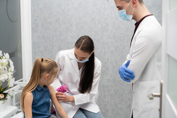 Fototapeta premium A nurse is getting ready to inject a little girl with a previously prepared vaccine. The young apprentice tries to talk to the child so that she is not afraid of the injection.