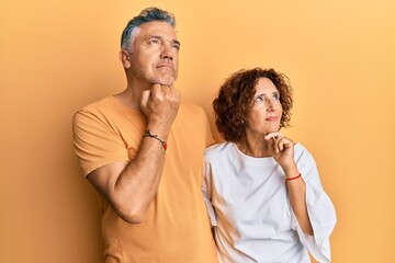 Beautiful middle age couple together wearing casual clothes with hand on chin thinking about question, pensive expression. smiling with thoughtful face. doubt concept.