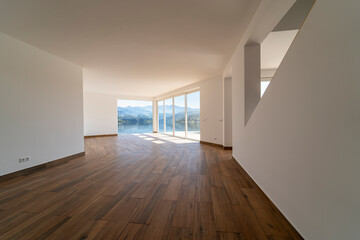 Fototapeta premium Empty room with dark wooden floating laminate flooring. House interior, wide bedroom space. New house or apartment by the lake with lake view. Wood floor. Real state or property management