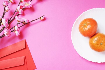 Chinese New Year 2021 background. Cherry blossom branch, two red envelopes and a plate with two tangerines on a table. Oriental traditions. Flat lay composition photography top view