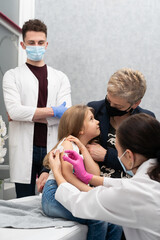 Grandma cheers her granddaughter during the vaccination. A young nurse stabs a needle into the...