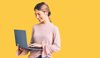 Naklejka premium Beautiful caucasian woman with blonde hair working using computer laptop looking positive and happy standing and smiling with a confident smile showing teeth