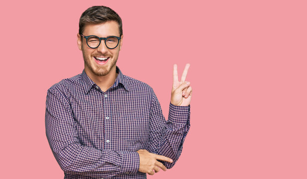 Handsome caucasian man wearing casual clothes and glasses smiling with happy face winking at the camera doing victory sign. number two.