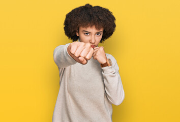 Young hispanic girl wearing wool winter sweater punching fist to fight, aggressive and angry...