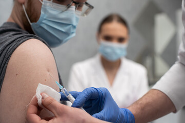 A nurse gives an injection to a patient with the COVID19 vaccine. A sterile doctor's office in a private clinic. A young medical intern looks at how to properly inject.