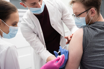 A young intern learns to inject a COVID19 vaccine into a young adult patient. A sterile doctor's office in a private clinic. A young nurse teaches a medical intern how to properly inject.