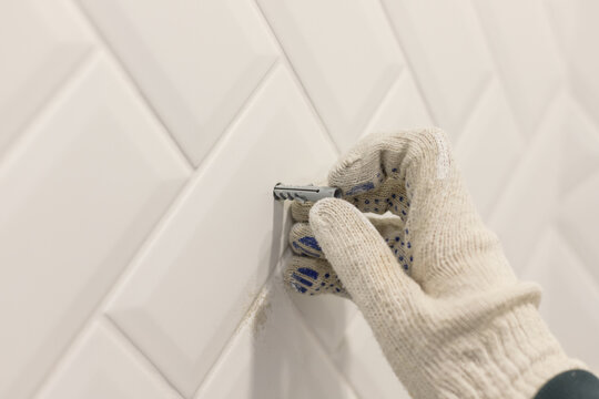 Worker's hand in glove inserts wall pvc dowel in wall cladded with tile ceramic