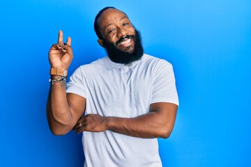 Naklejka premium Young african american man wearing casual white tshirt smiling with happy face winking at the camera doing victory sign. number two.