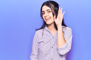 Young beautiful girl wearing casual striped shirt smiling with hand over ear listening and hearing to rumor or gossip. deafness concept.