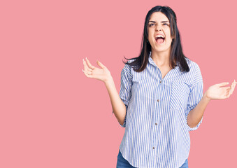 Young beautiful girl wearing striped shirt crazy and mad shouting and yelling with aggressive expression and arms raised. frustration concept.