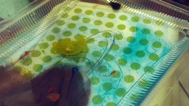 Child with father making marble patterns with paint and brush on water surface. Ebru art. close up
