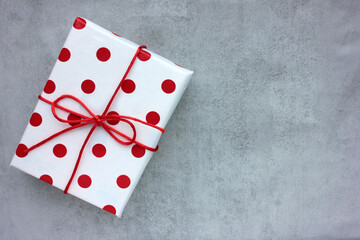 Gift box in wrapping paper with red polka dot pattern on gray concrete background. Top view, copy space