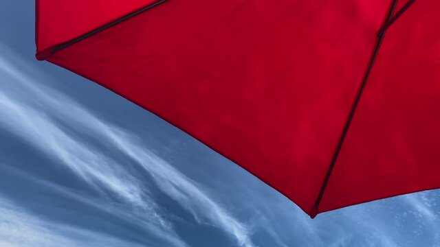 A red parasol umbrella is seen against the blue sky and clouds is lit with the sun&rsquo;s refection off of the water's surface. 